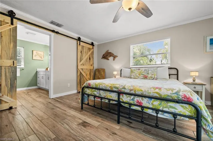 Bedroom featuring a barn door, ornamental molding, ceiling fan, and wood finished floors