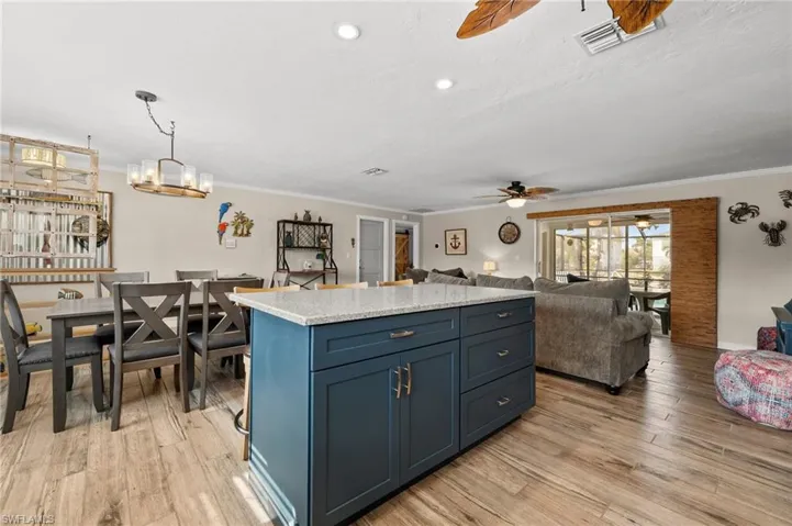 Kitchen featuring blue cabinetry, hanging light fixtures, light stone counters, open floor plan, and light wood finished floors