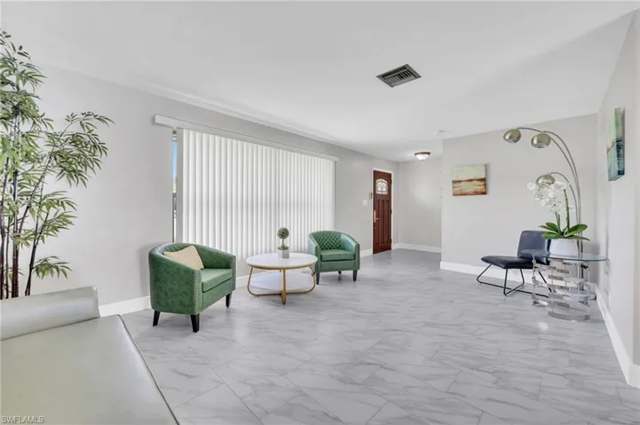 Spacious living area featuring large format tile flooring, crown molding, and a wide window with vertical blinds