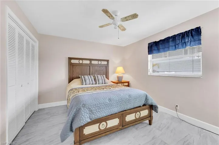 Sleeping area featuring light gray tile flooring, a window with horizontal blinds, and a ceiling fan with light fixture