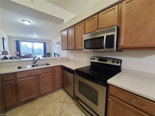 Kitchen featuring stainless steel appliances, brown cabinets, light countertops, light tile patterned floors, and open floor plan