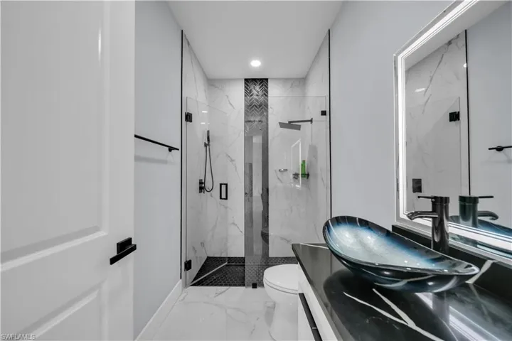 Bathroom featuring vanity, a marble finish shower, light marble finish flooring, and recessed lighting