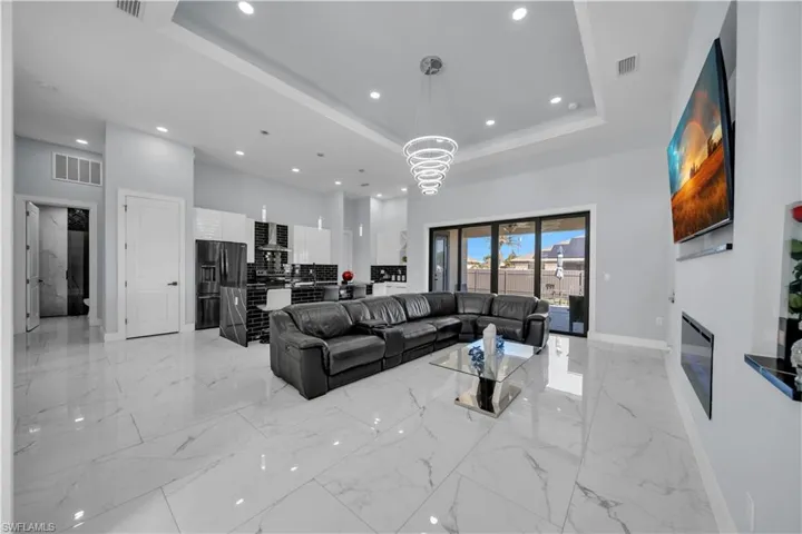 Living room with a high tray ceiling, suspended lighting, a glass covered fireplace, and light marble finish flooring