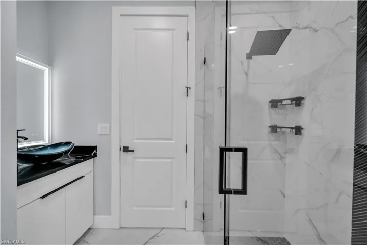 Full bathroom featuring vanity, a marble finish shower, and light marble finish floors