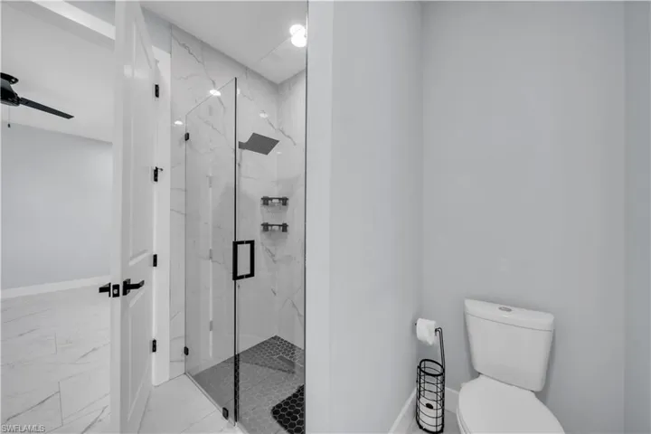 Bathroom with a marble finish shower, marble look tile flooring, and a ceiling fan