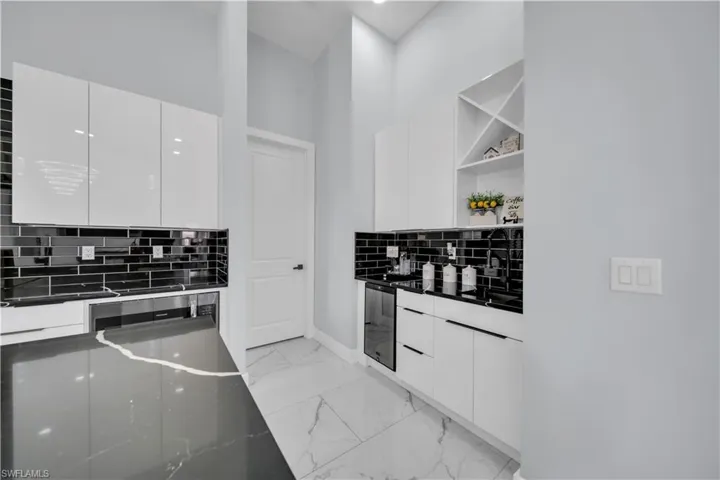 Kitchen featuring modern cabinets, white cabinetry, backsplash, dark stone countertops, and light marble finish floors