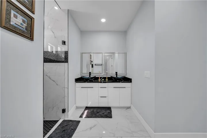Bathroom with double vanity, a marble finish shower, light marble finish floors, and recessed lighting