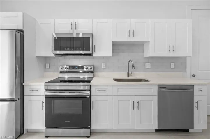 Kitchen with appliances with stainless steel finishes, decorative backsplash, white cabinets, and light stone counters