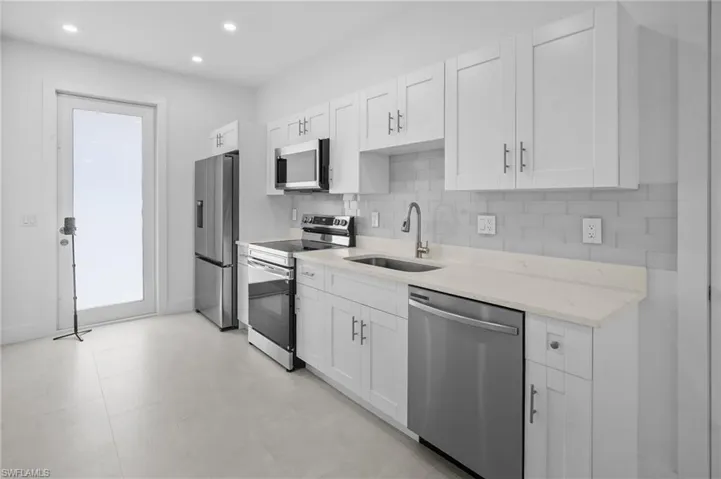 Kitchen featuring decorative backsplash, appliances with stainless steel finishes, light stone counters, white cabinets, and recessed lighting