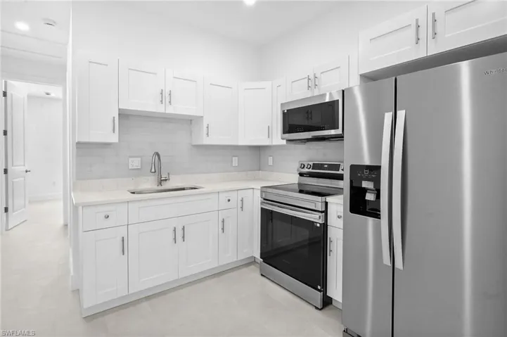 Kitchen featuring stainless steel appliances, white cabinets, backsplash, light stone counters, and recessed lighting
