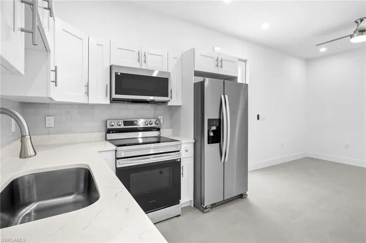 Kitchen featuring appliances with stainless steel finishes, backsplash, white cabinetry, light stone counters, and recessed lighting