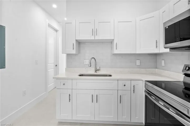 Kitchen featuring stainless steel appliances, backsplash, white cabinetry, light stone countertops, and recessed lighting