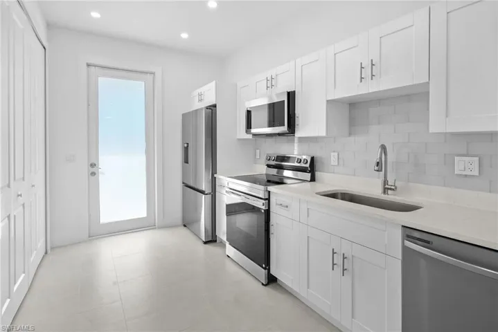 Kitchen featuring appliances with stainless steel finishes, light stone countertops, decorative backsplash, white cabinetry, and recessed lighting