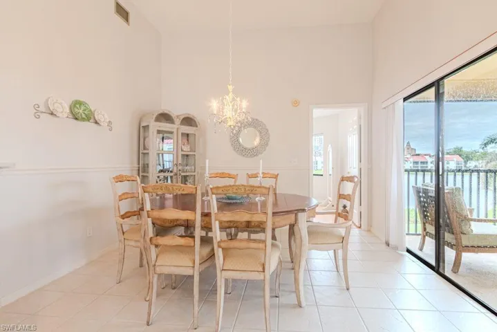 Dining area with light tile patterned floors, a towering ceiling, a water view, and a notable chandelier