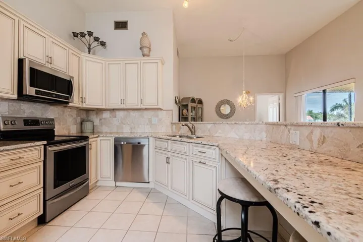 Kitchen featuring cream cabinets, sink, light stone countertops, decorative light fixtures, and stainless steel appliances