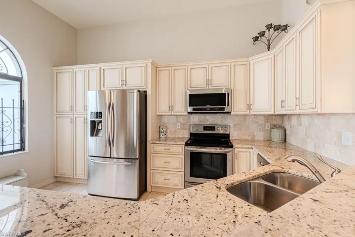 Kitchen featuring light stone countertops, sink, stainless steel appliances, cream cabinets, and decorative backsplash