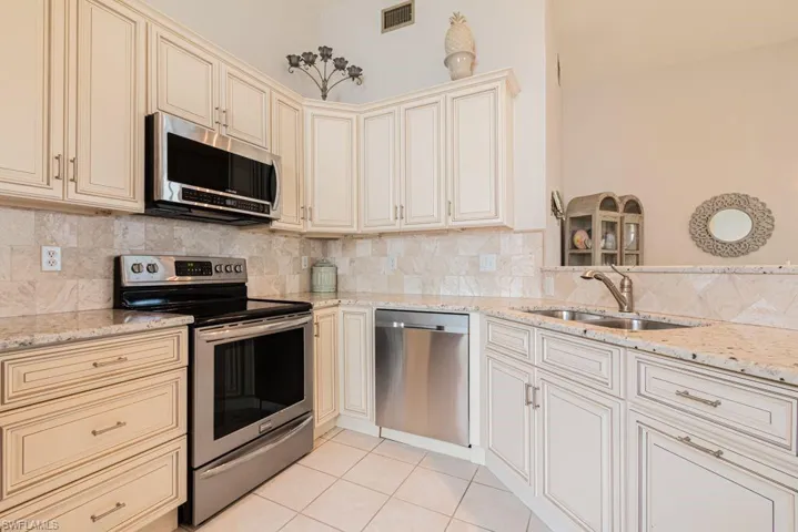 Kitchen featuring light stone countertops, appliances with stainless steel finishes, cream cabinets, and sink