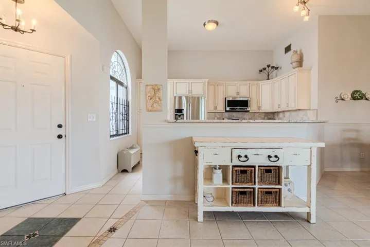 Kitchen with kitchen peninsula, stainless steel appliances, an inviting chandelier, cream cabinetry, and light tile patterned flooring