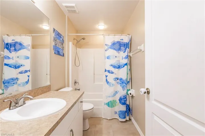 Bathroom with tile patterned flooring, vanity, toilet, visible vents, and shower / bath combo with shower curtain