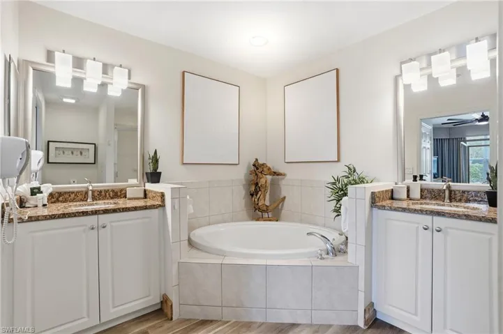 Full bathroom with a bath, two vanities, a shower stall, and light wood finished floors