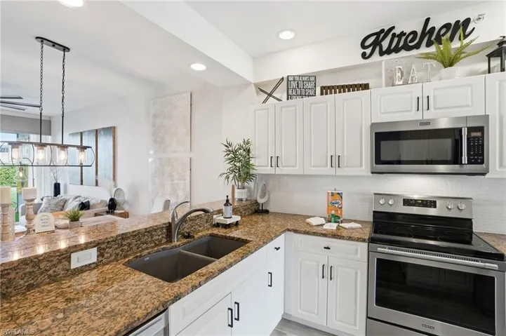 Kitchen with appliances with stainless steel finishes, backsplash, open floor plan, white cabinets, and dark stone countertops