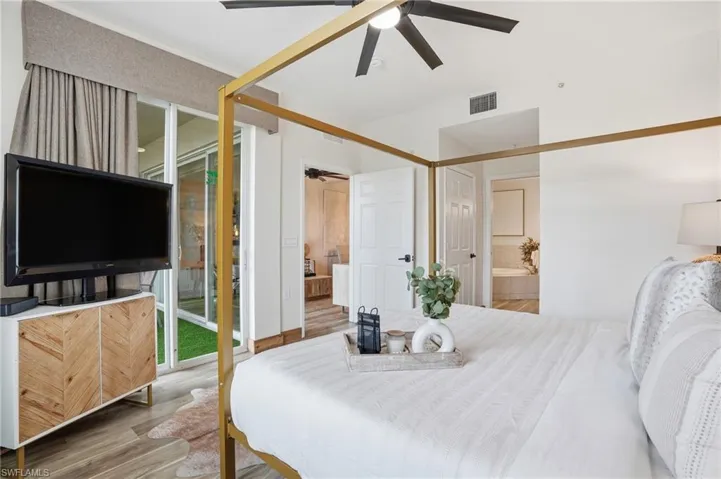 Bedroom with wood finished floors, ceiling fan, ensuite bathroom, and access to exterior
