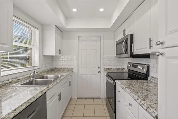 Kitchen featuring appliances with stainless steel finishes, white cabinetry, light tile patterned floors, recessed lighting, and a raised ceiling