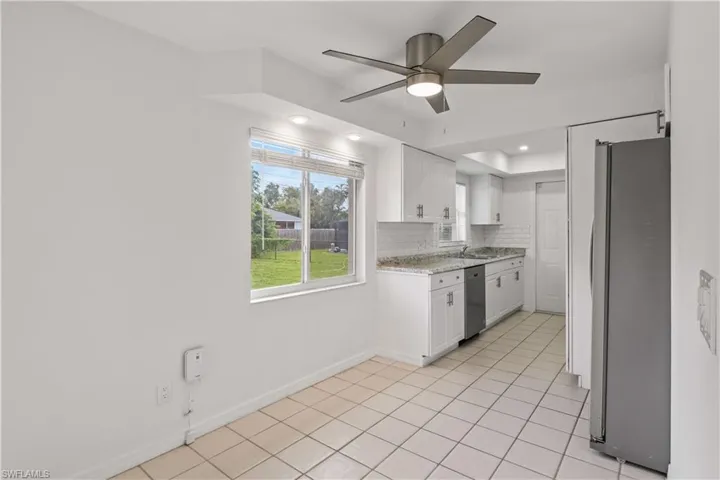 Kitchen featuring white cabinets, appliances with stainless steel finishes, light tile patterned floors, backsplash, and a ceiling fan