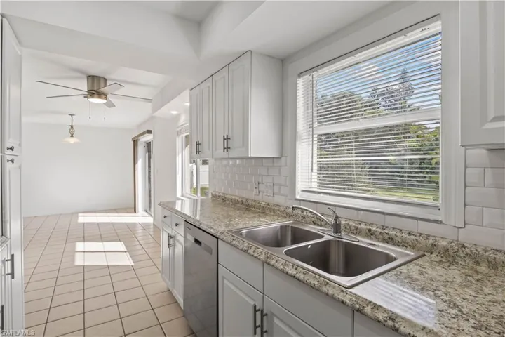 Kitchen with light tile patterned floors, ceiling fan, dishwasher, white cabinets, and plenty of natural light
