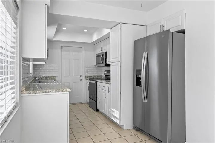 Kitchen featuring stainless steel appliances, white cabinetry, light tile patterned flooring, decorative backsplash, and recessed lighting