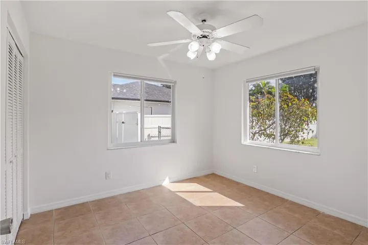 Unfurnished bedroom with light tile patterned floors, ceiling fan, multiple windows, and a closet
