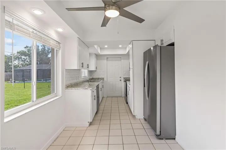 Kitchen featuring appliances with stainless steel finishes, backsplash, white cabinetry, light tile patterned floors, and light stone countertops