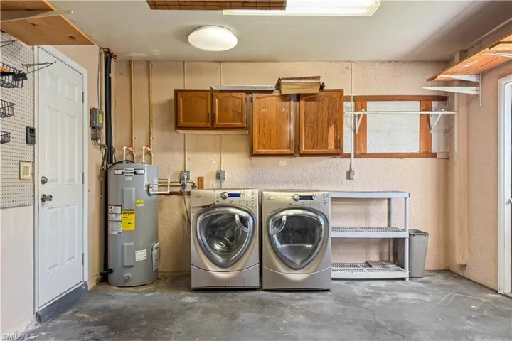 Washroom with concrete flooring, water heater, independent washer and dryer, cabinet space, and a textured wall