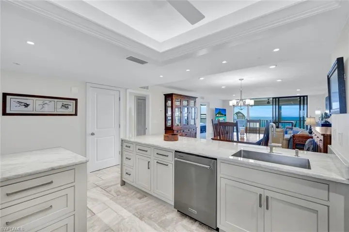 Kitchen with light stone counters, dishwasher, open floor plan, a ceiling fan, and suspended lighting