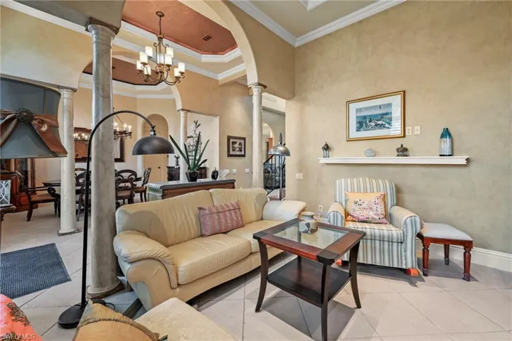 Living area featuring crown molding, a chandelier, decorative columns, arched walkways, and tile patterned flooring
