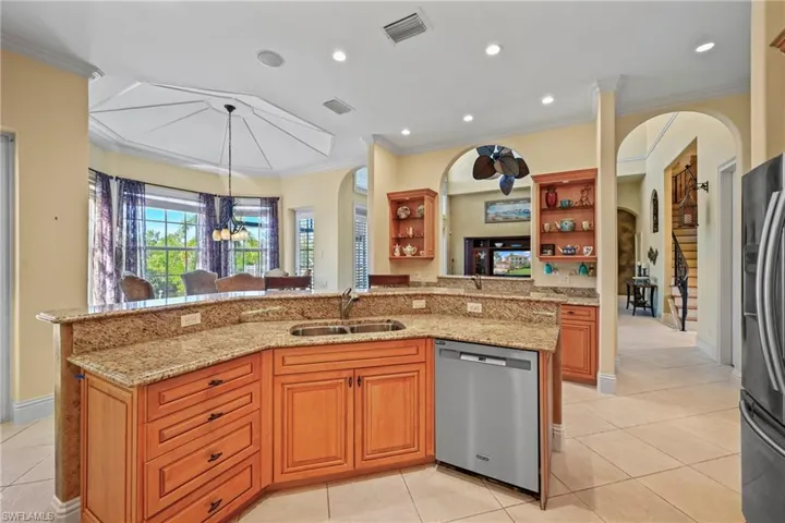 Kitchen with a chandelier, appliances with stainless steel finishes, light stone counters, crown molding, and arched walkways