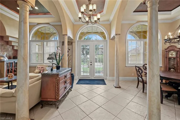 Entryway with a raised ceiling, ornate columns, ornamental molding, a chandelier, and healthy amount of natural light