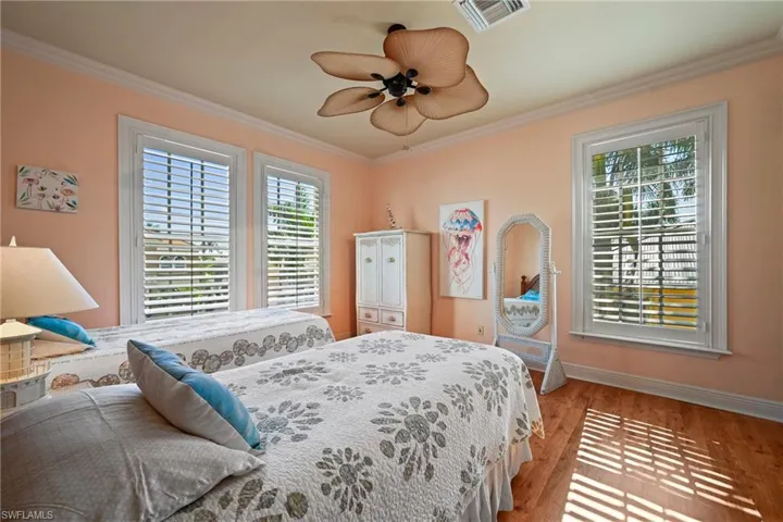 Bedroom with wood finished floors, multiple windows, crown molding, and a ceiling fan
