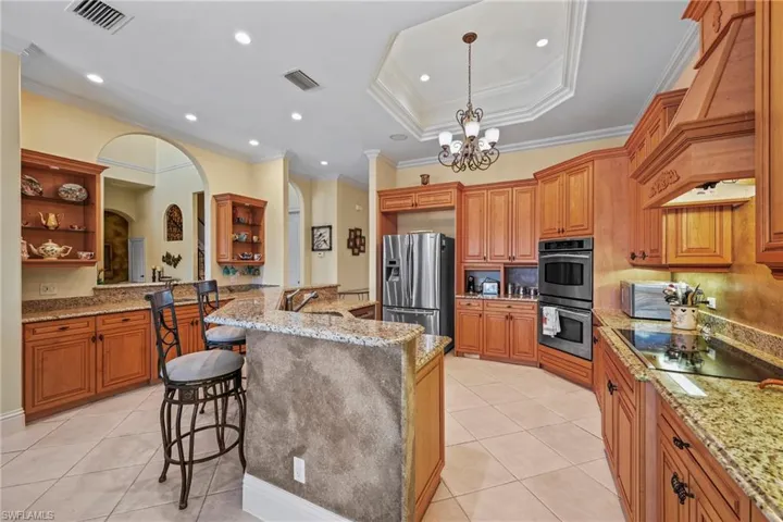 Kitchen with a kitchen bar, light tile patterned floors, crown molding, brown cabinetry, and stainless steel appliances