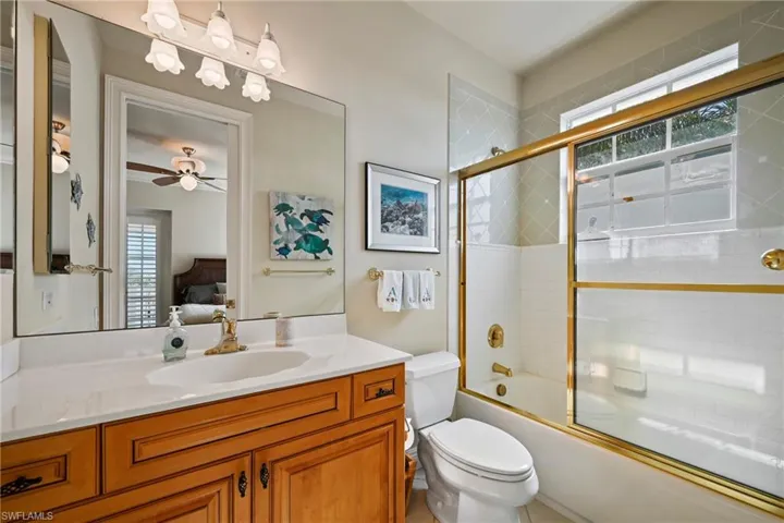 Full bath with shower / bath combination with glass door, ensuite bathroom, vanity, and a ceiling fan