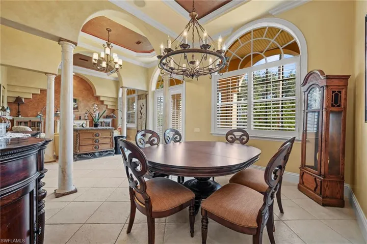 Dining space featuring decorative columns, crown molding, a tray ceiling, light tile patterned floors, and arched walkways