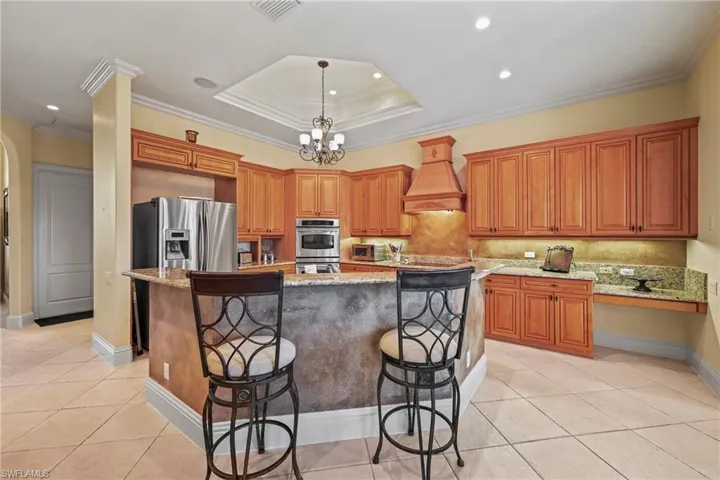 Kitchen with light stone countertops, a kitchen bar, light tile patterned flooring, pendant lighting, and ornamental molding