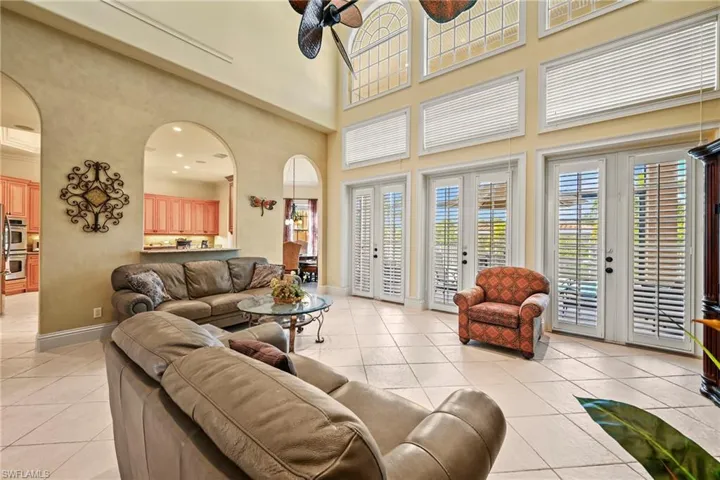 Living area featuring arched walkways, light tile patterned flooring, a ceiling fan, a high ceiling, and french doors