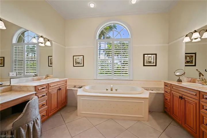 Bathroom with two vanities, a bath, healthy amount of natural light, and crown molding