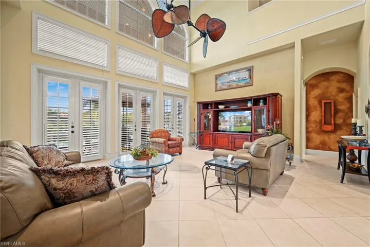 Living room with arched walkways, light tile patterned floors, a ceiling fan, and a towering ceiling