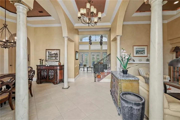 Foyer featuring a chandelier, a raised ceiling, tile patterned floors, ornate columns, and a towering ceiling