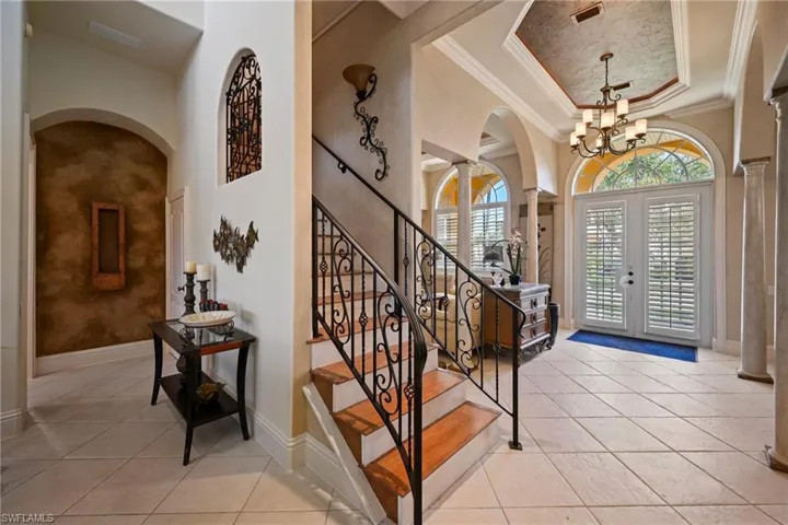 Entryway featuring a raised ceiling, crown molding, light tile patterned floors, french doors, and ornate columns