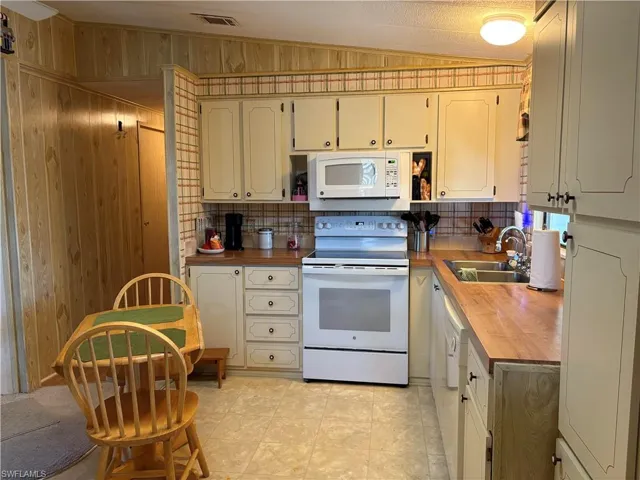 Kitchen featuring butcher block counters, white appliances, vaulted ceiling, wood walls, and sink