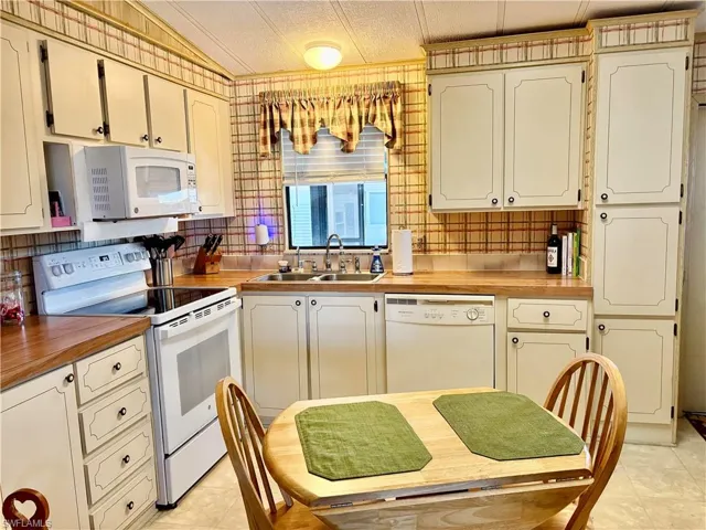 Kitchen with white appliances, lofted ceiling, sink, light tile patterned flooring, and butcher block countertops