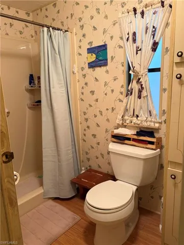 Bathroom with a shower with shower curtain, toilet, and hardwood / wood-style floors